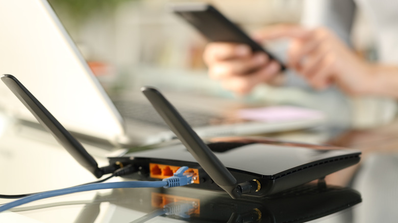 A close-up view of the rear of a Wi-Fi router, with a blurred image of a smartphone in the rear.