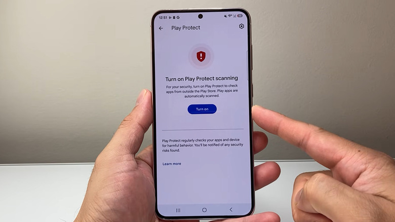 A man holding an Android shows a settings page, where he can "turn on Play Protect scanning."