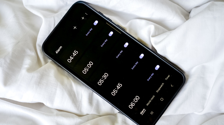 Phone showing early morning alarms on white bed sheets.