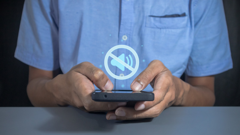 Man holding phone with mute sound symbol.