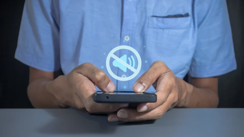 Man holding phone with mute sound symbol.