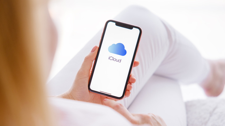 Person holding an iPhone with the iCloud logo showing.