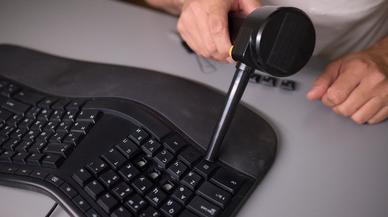 A hand using a compressed air tool to clean a keyboard.
