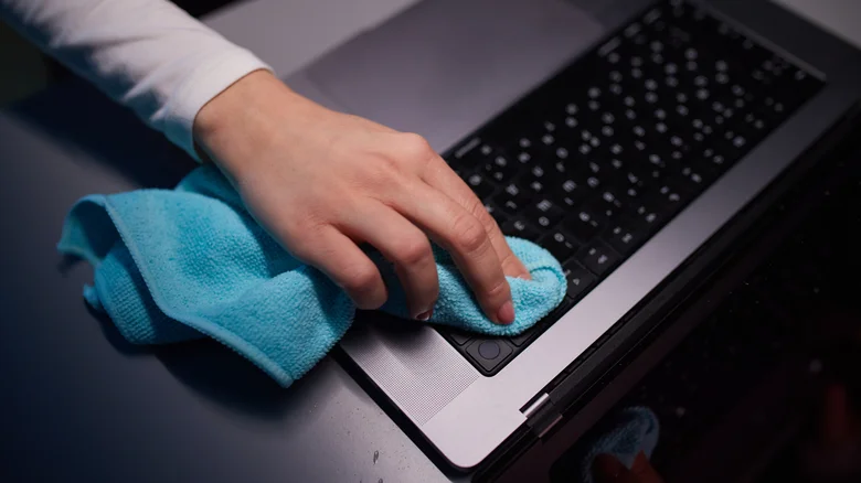 Hand cleaning a laptop keyboard with a microfiber cloth.