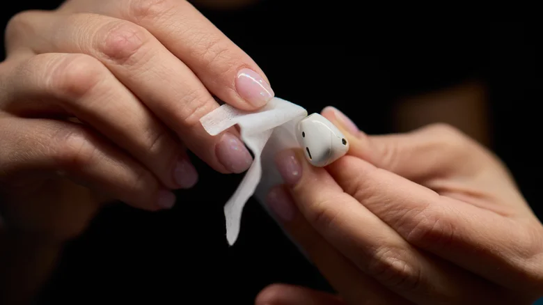 Two hands wiping down a pair of wireless earbuds.