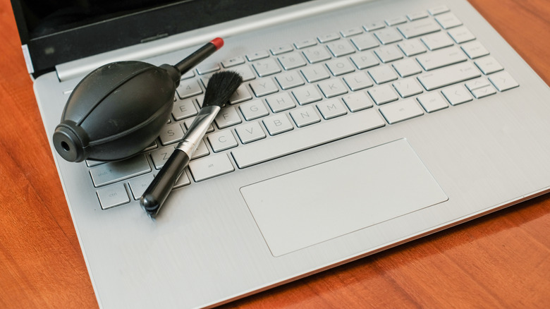 A bulb blower and cleaning brush resting on a laptop keyboard.