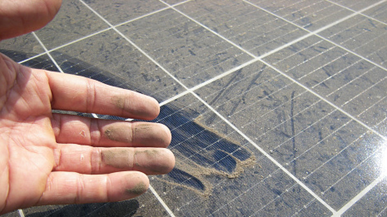 A hand with dust-covered fingers held over a dirty solar panel.