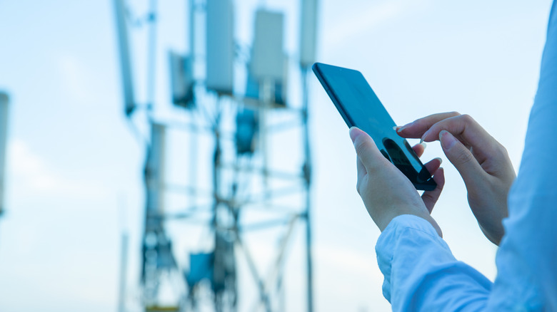 Hands interacting with a smartphone, with a cellular tower in the background.