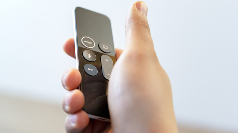 A hand holding an Apple TV remote on a white background.