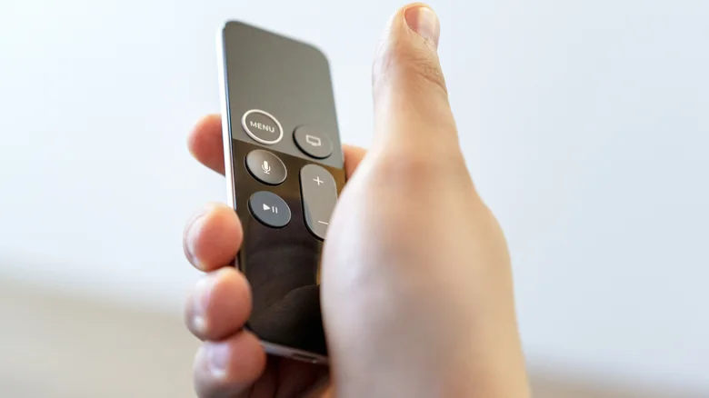 A hand holding an Apple TV remote on a white background.