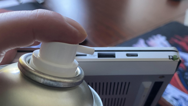 A can of compressed air hovering over a USB port on a laptop