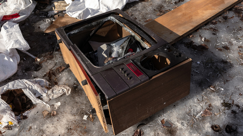 A broken vintage TV at a garbage dump with missing glass.