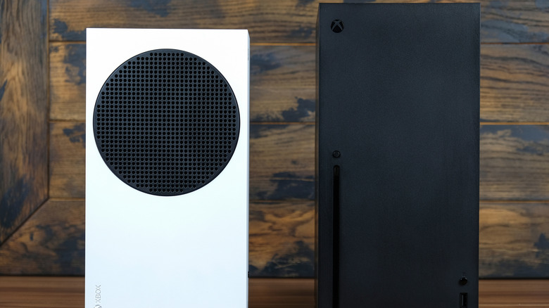 An Xbox Series S next to an Xbox Series X with a wood background.