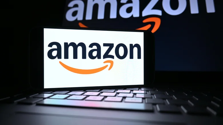 Phone screen displaying the Amazon logo with an open laptop displaying the same in the background.