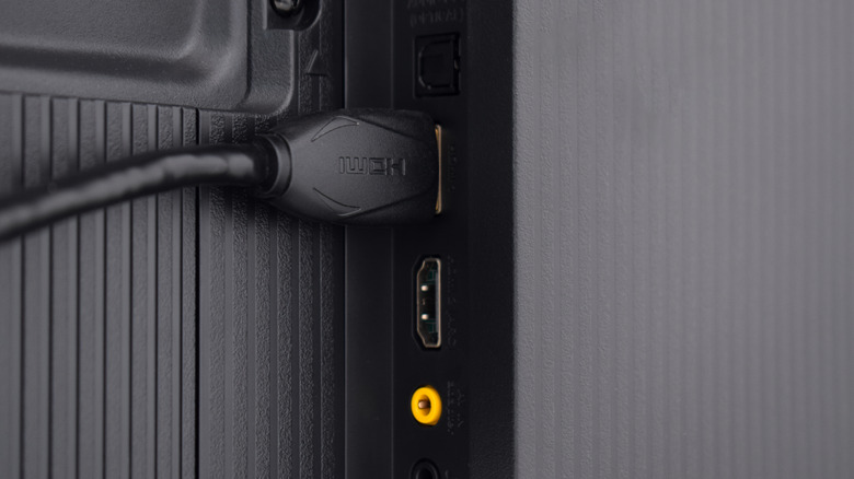 Um cabo HDMI conectado &agrave; parte traseira de uma TV, junto com v&aacute;rias outras portas.