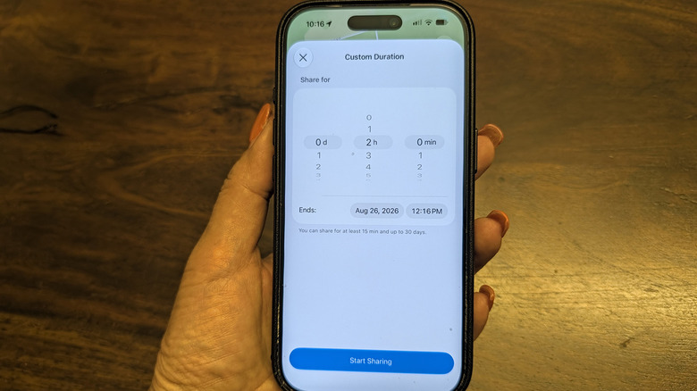 A hand holding an iPhone showing a custom duration for sharing your location with someone in Find My.