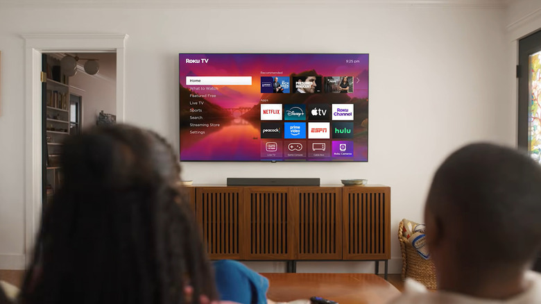 Seen from behind, a couple looks at their new Roku TV's home screen.