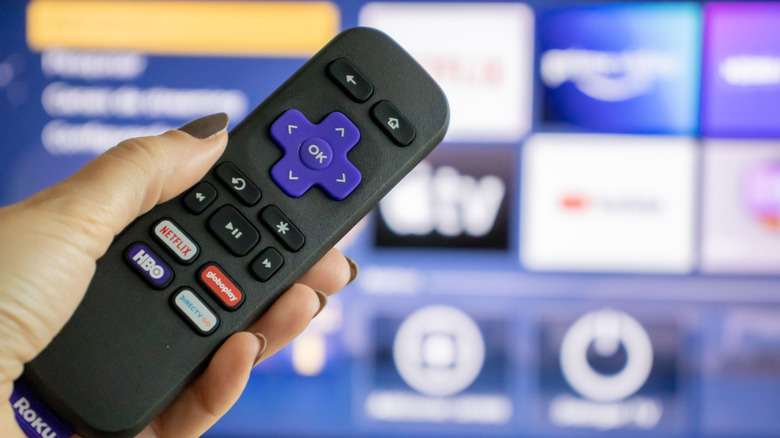 A person points Roku's iconic remote at the old Roku home screen.