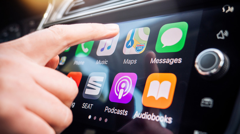 A finger touching a screen to open Maps in CarPlay.