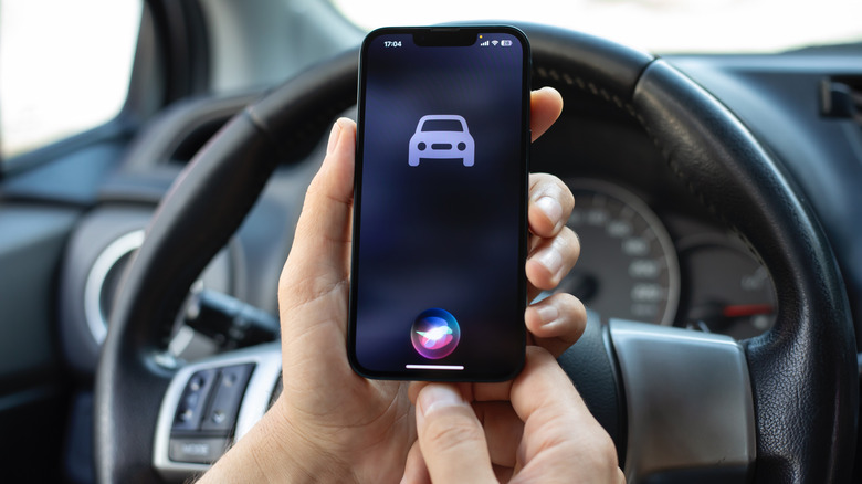 A car icon showing on an iPhone with Siri activated, in front of a steering wheel.