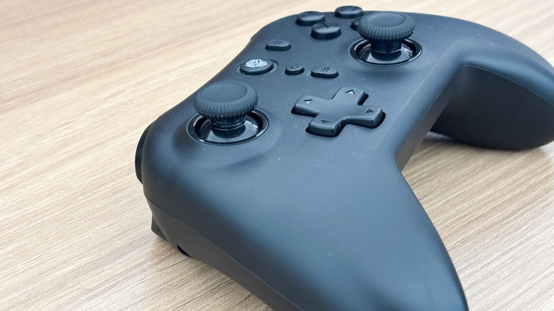 A black Bluetooth gaming controller on wooden surface.