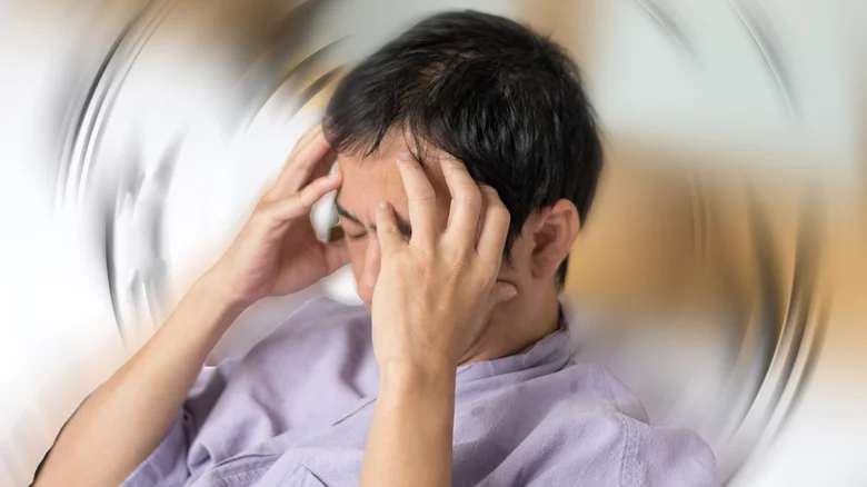 A man holds his head in his hands in front of a blurred, swirling background.