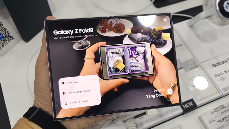 A hand holds a Samsung Galaxy Z Fold8 in a store display while the inner screen shows promotional content for the phone.