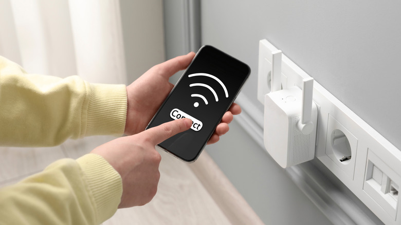 Wi-Fi extender plugged into an outlet and a person checking phone signal.