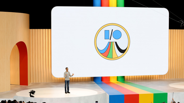 Alphabet CEO Sundar Pichai stands on stage in front of a large screen that has a Google I/O logo.