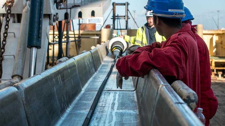 Workers running a long cable along a metal runway on a ship
