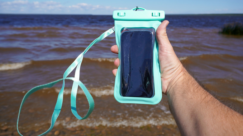 A hand holding a smartphone in a waterproof bag at the beach.