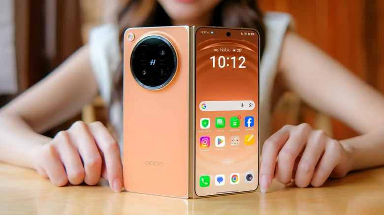 Woman showing the Oppo Find N6 foldable phone, with its outer screen, orange back and camera setup.