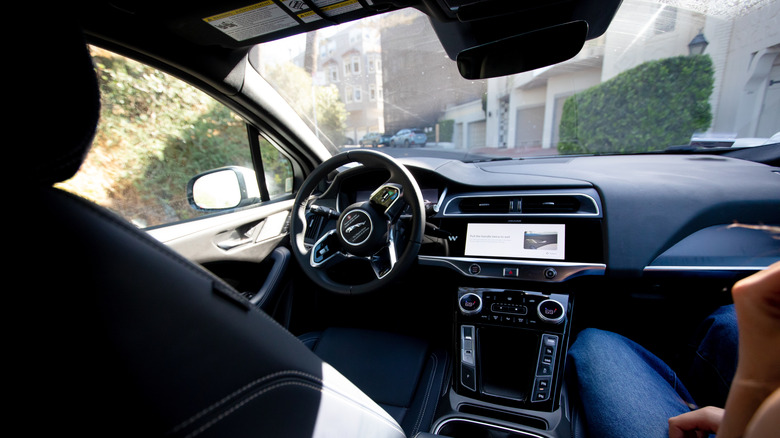 Interior of a Waymo self-driving Jaguar with an empty driver's seat, steering wheel and dashboard visible from the rear passenger area.