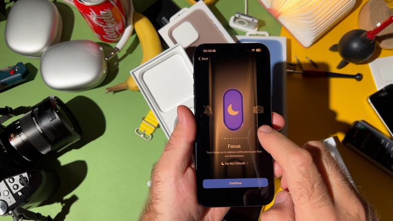 An iPhone using the Action Button to change Focus modes, on top of a cluttered table.