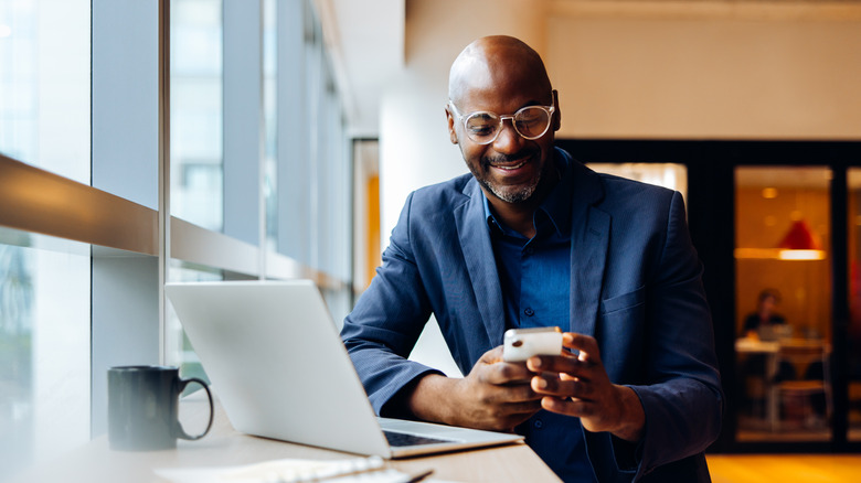 Man using a smartphone while working on his laptop.