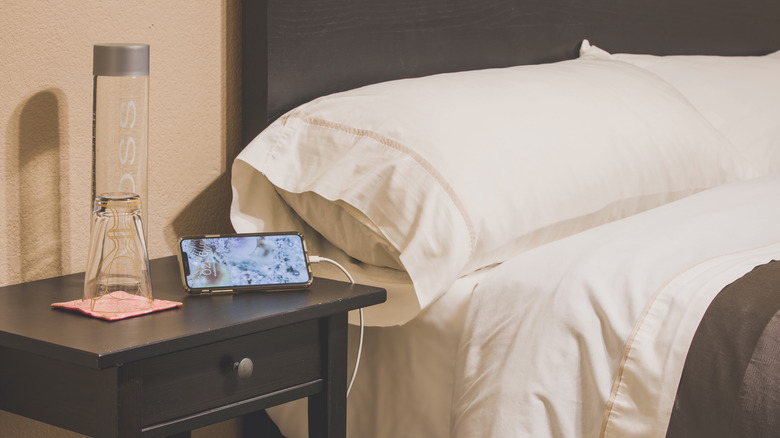 An iPhone charging on a nightstand next to a bed.