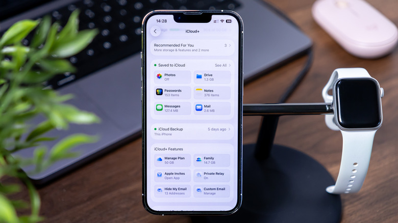 An iPhone showing iCloud settings on a charging stand next to an Apple Watch.