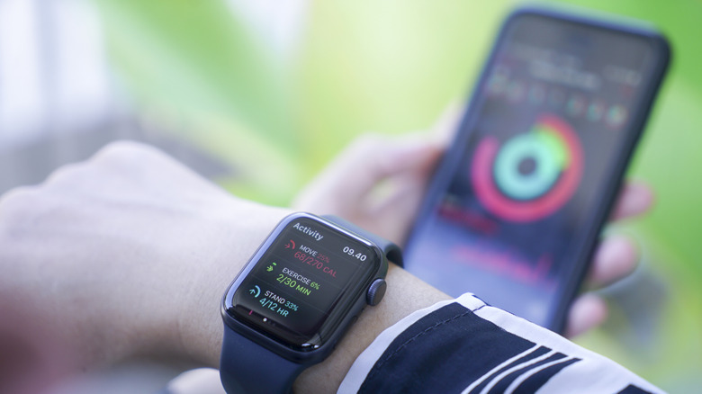 An Apple Watch with the Activity screen up and a blurred background view of an iPhone, also with an Activity screen up.