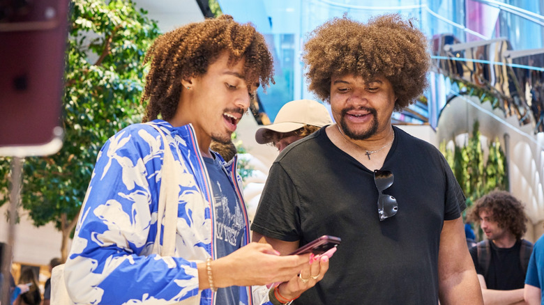 Two men staring at an iPhone held by the man in a blue shirt.
