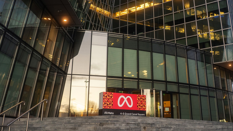 Meta's logo against a red background in front of an office building.