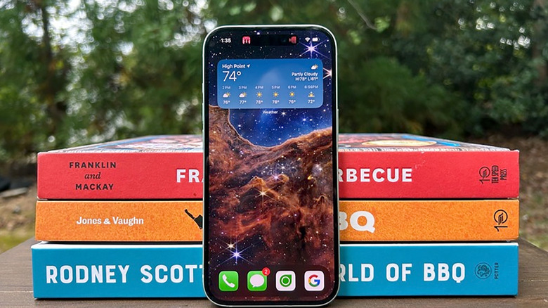 An iPhone 15 propped up against three books.