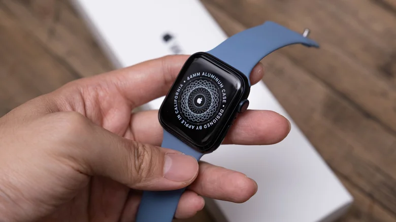 The back of a new Apple Watch with a light blue strap, in front of its box.