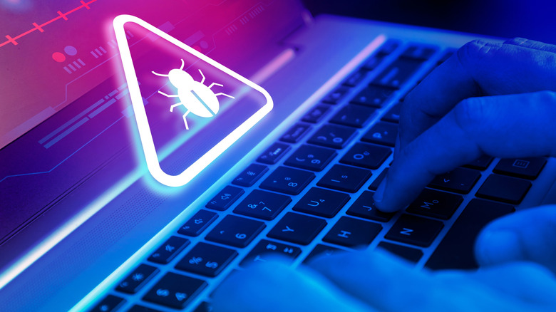 Fingers typing on a laptop with a bug icon inside a triangle above, indicating a threat.