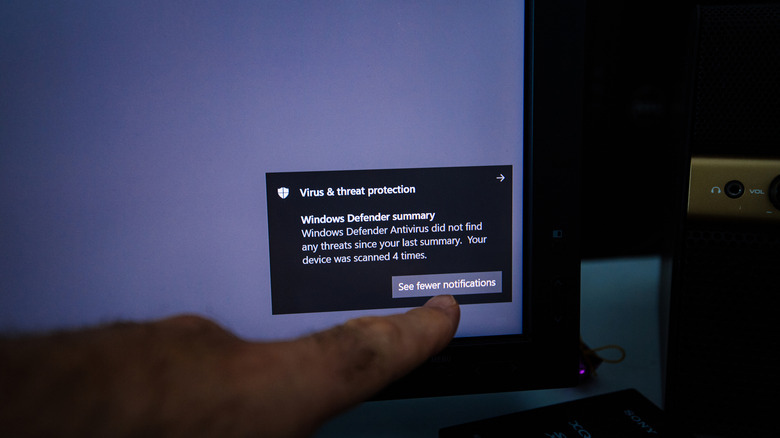 Finger pointing to a Microsoft Defender antivirus scan notification on a Windows 10 system.