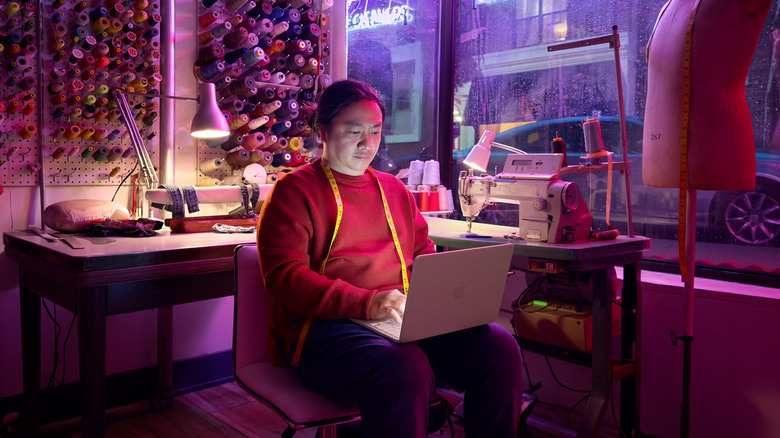 A man in a room with red lighting working on a MacBook Neo.