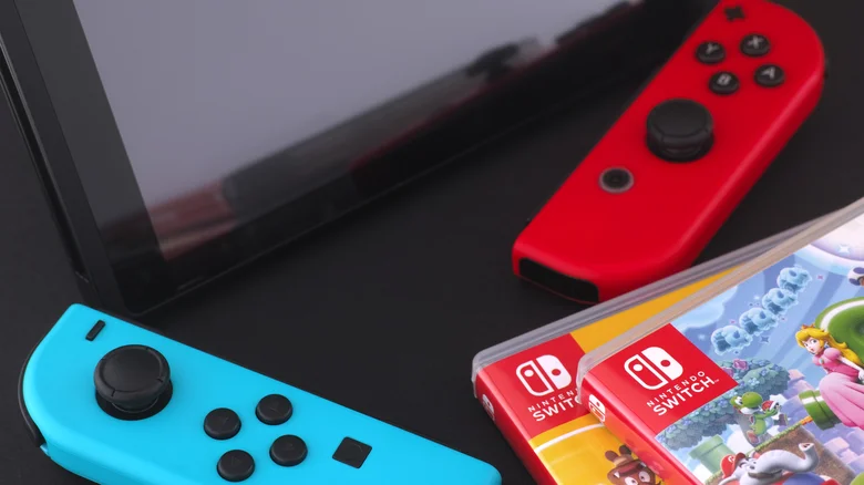 A Nintendo Switch console with joy-cons near a stack of Nintendo Switch games in boxes.