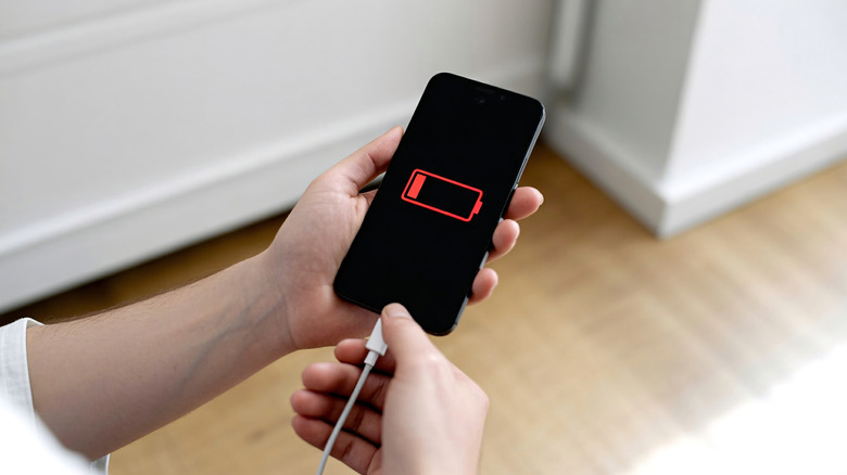 Hands hold a plugged-in smart phone with a low battery screen.