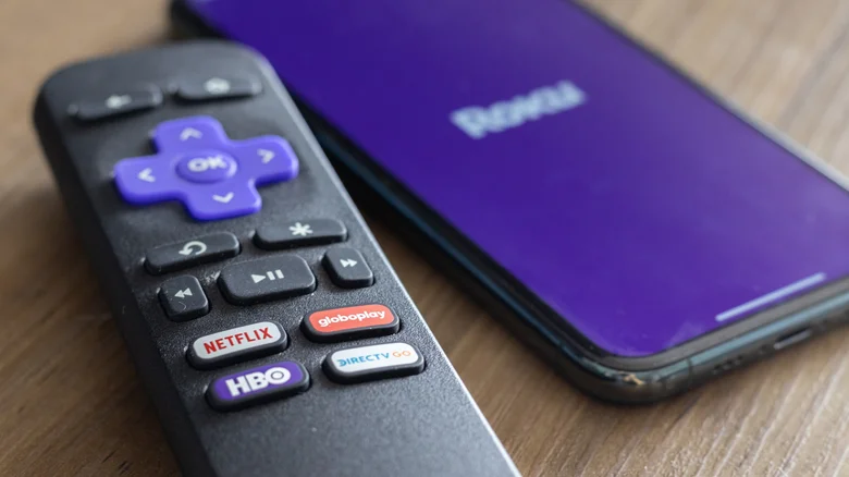 A close-up shot of a Roku remote and a phone running the Roku app.