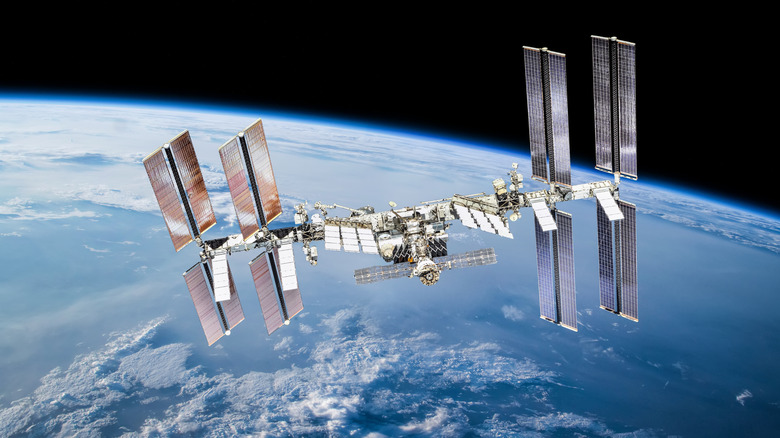 The ISS floats in space, the Earth and sun behind it.