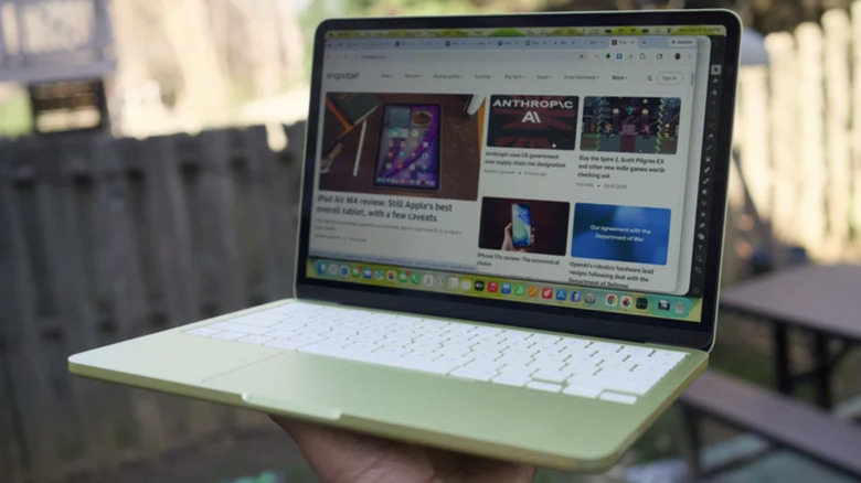 A citrus MacBook Neo being held up with one hand.